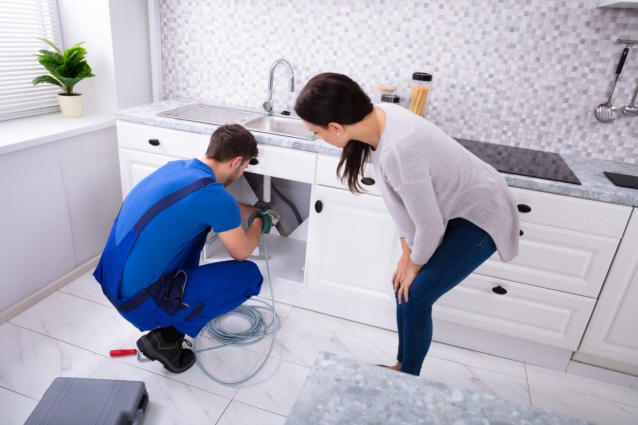 Woman watching plumber fix pipes under sink