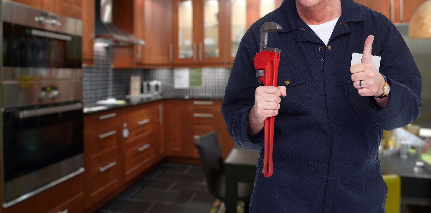 Plumber holding red wrench and giving a thumbs up in a kitchen